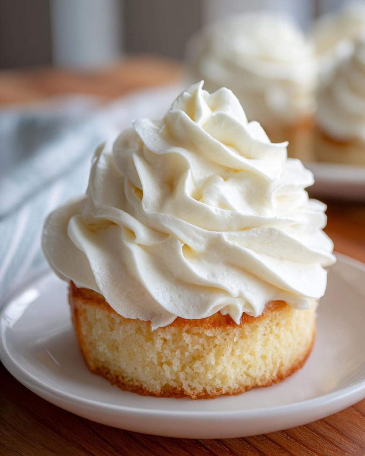 Close-up of a small vanilla cake topped with a generous swirl of fluffy vanilla buttercream frosting.