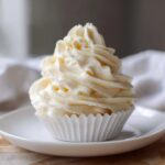 A single cupcake topped with a tall swirl of fluffy vanilla buttercream frosting.
