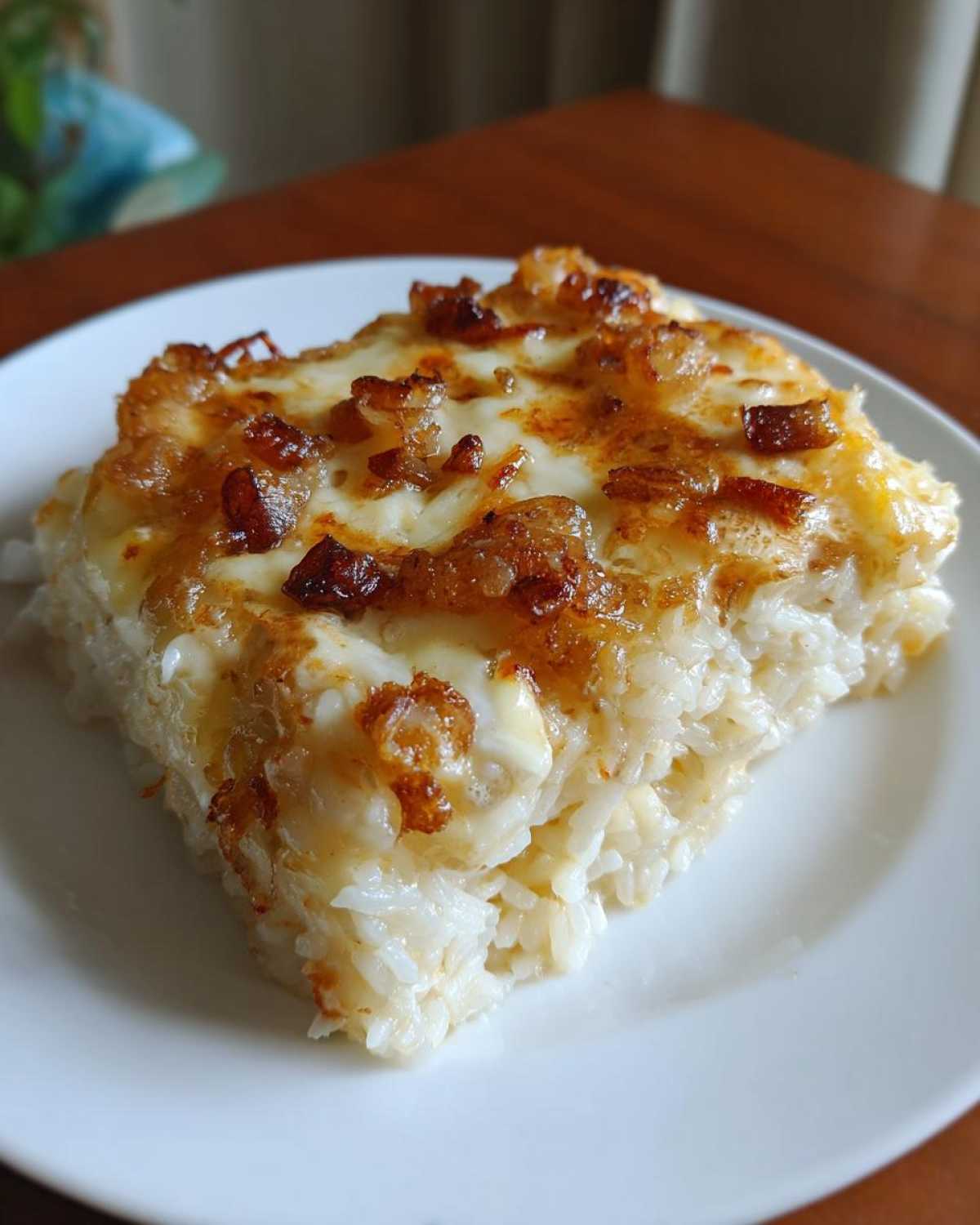A square serving of baked french onion butter rice topped with melted cheese and caramelized onions.
