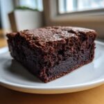 Close-up of a rich, fudgy square of sweet potato brownies with a crackly top, served on a white plate.