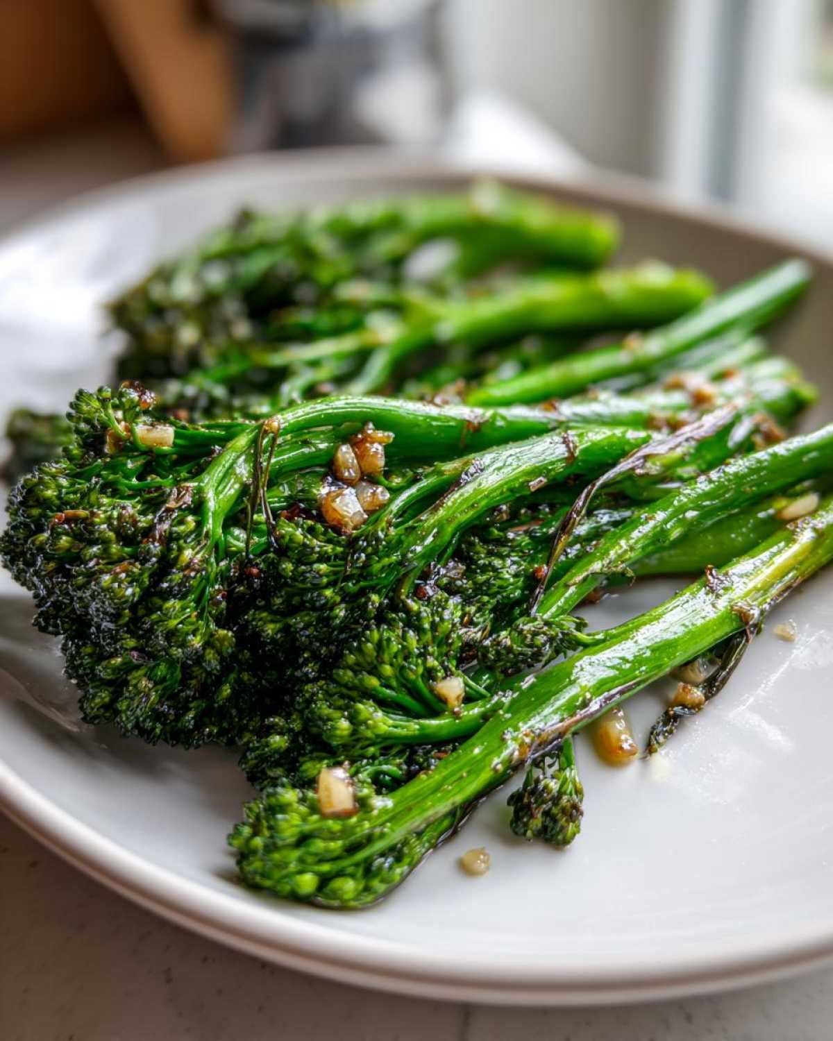 Close-up of bright green, sautéed broccolini tossed with visible pieces of garlic on a white plate.