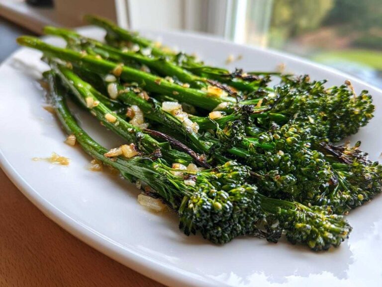 A close-up of perfectly cooked garlic lemon broccolini served on a white plate.