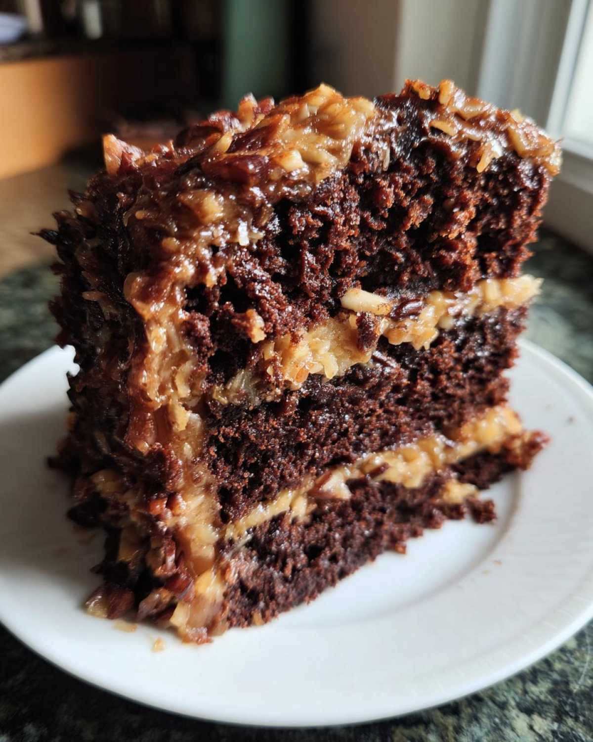 Close-up of a moist slice of German chocolate cake recipe with thick coconut-pecan frosting layers.
