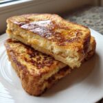 Close-up of two thick slices of golden brown easy french toast stacked on a white plate, glistening with syrup.