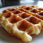 Close-up of two golden brown, fluffy high protein waffles resting on a white plate.