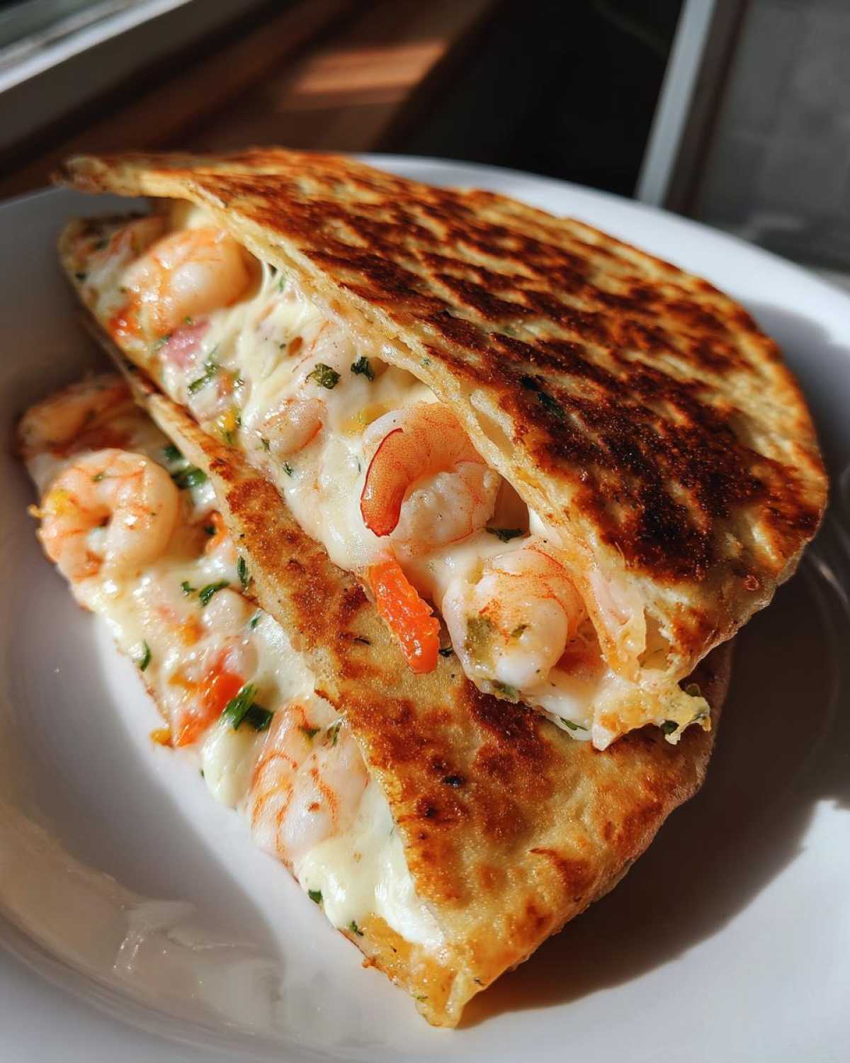 Close-up of a golden-brown shrimp quesadilla cut in half, overflowing with melted white cheese and pink shrimp.