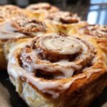 Close-up of a tray of gooey homemade cinnamon buns topped with thick white icing.