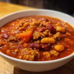 Close-up of a steaming bowl of rich, red high protein chili featuring ground meat, kidney beans, and white beans.