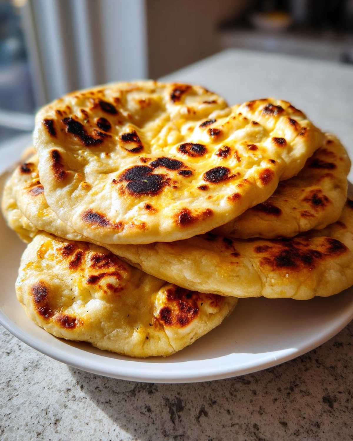 A stack of fluffy, golden homemade naan bread with characteristic charred bubbles, served on a white plate.