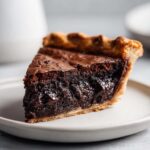 Close-up of a rich, fudgy slice of hot fudge pie with a flaky crust on a light plate.