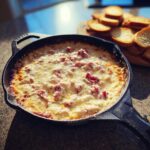 Hot, cheesy reuben dip bubbling in a cast iron skillet, served with toasted bread slices nearby.