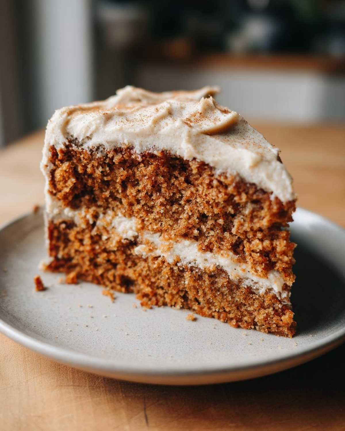 Close-up of a moist slice of applesauce cake layered with cream cheese frosting and dusted with cinnamon.