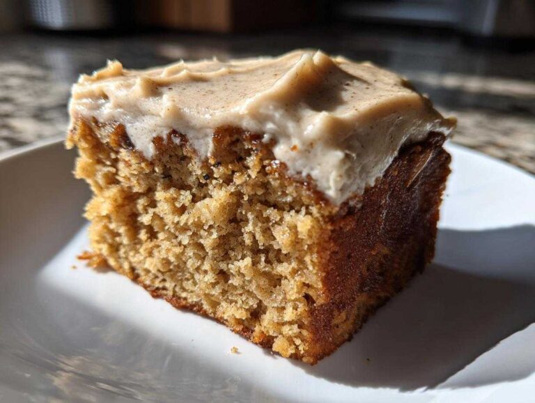 5 Amazing Moist Applesauce Cake Secrets Close-up of a moist slice of applesauce cake topped with thick, spiced cream cheese frosting.