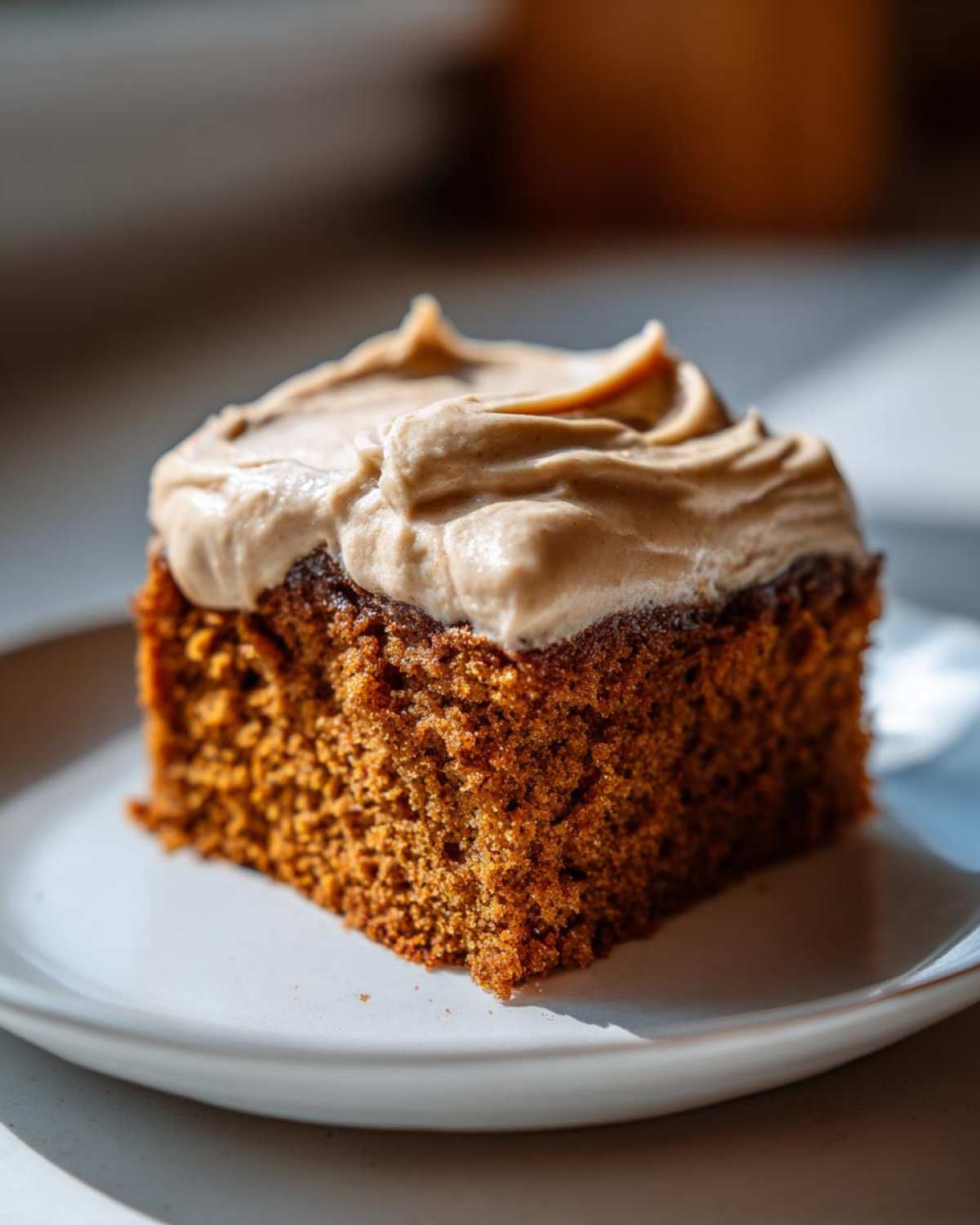 Close-up of a rich, moist slice of applesauce cake topped with thick, swirled brown sugar frosting.