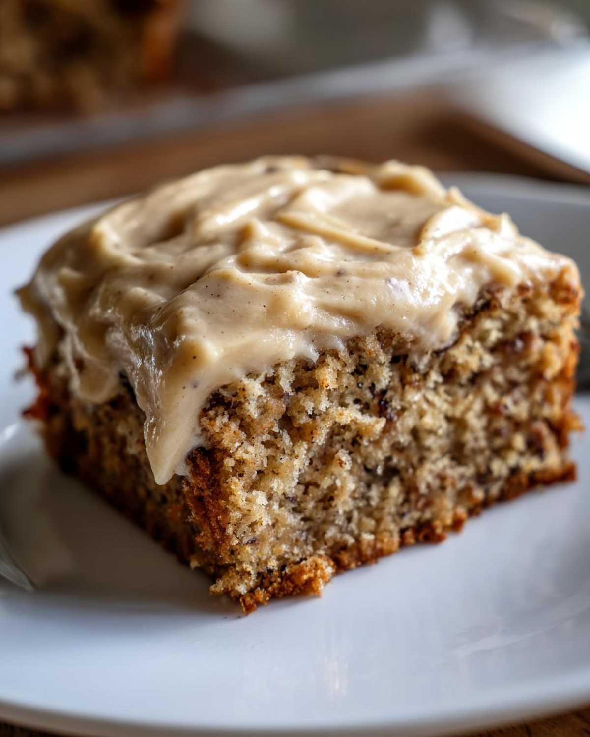 Close-up of a moist slice of applesauce cake topped with creamy, speckled brown butter frosting.
