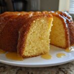 A slice cut from a moist Bacardi Rum Cake, drizzled heavily with a golden rum glaze on a white plate.