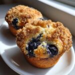 Close-up of two moist blueberry muffins topped with a golden brown streusel crumb topping.