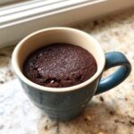 A moist chocolate mug cake baked perfectly inside a blue ceramic mug.