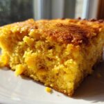 Close-up of a moist, golden slice of cornbread casserole showing corn kernels embedded in the texture.