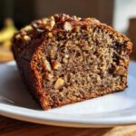 Close-up of a moist slice of date nut bread showing the dense crumb and chopped walnuts on top.