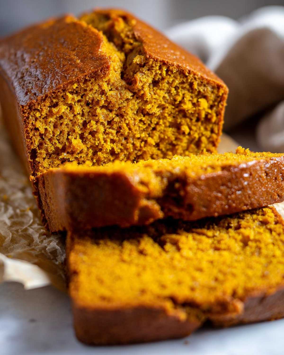 Close-up of moist pumpkin bread loaf with two thick slices cut and resting against it.