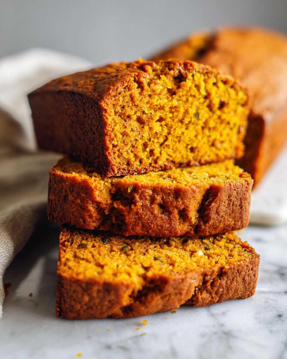 Three thick slices of moist pumpkin bread stacked on a marble surface, showing the rich orange crumb