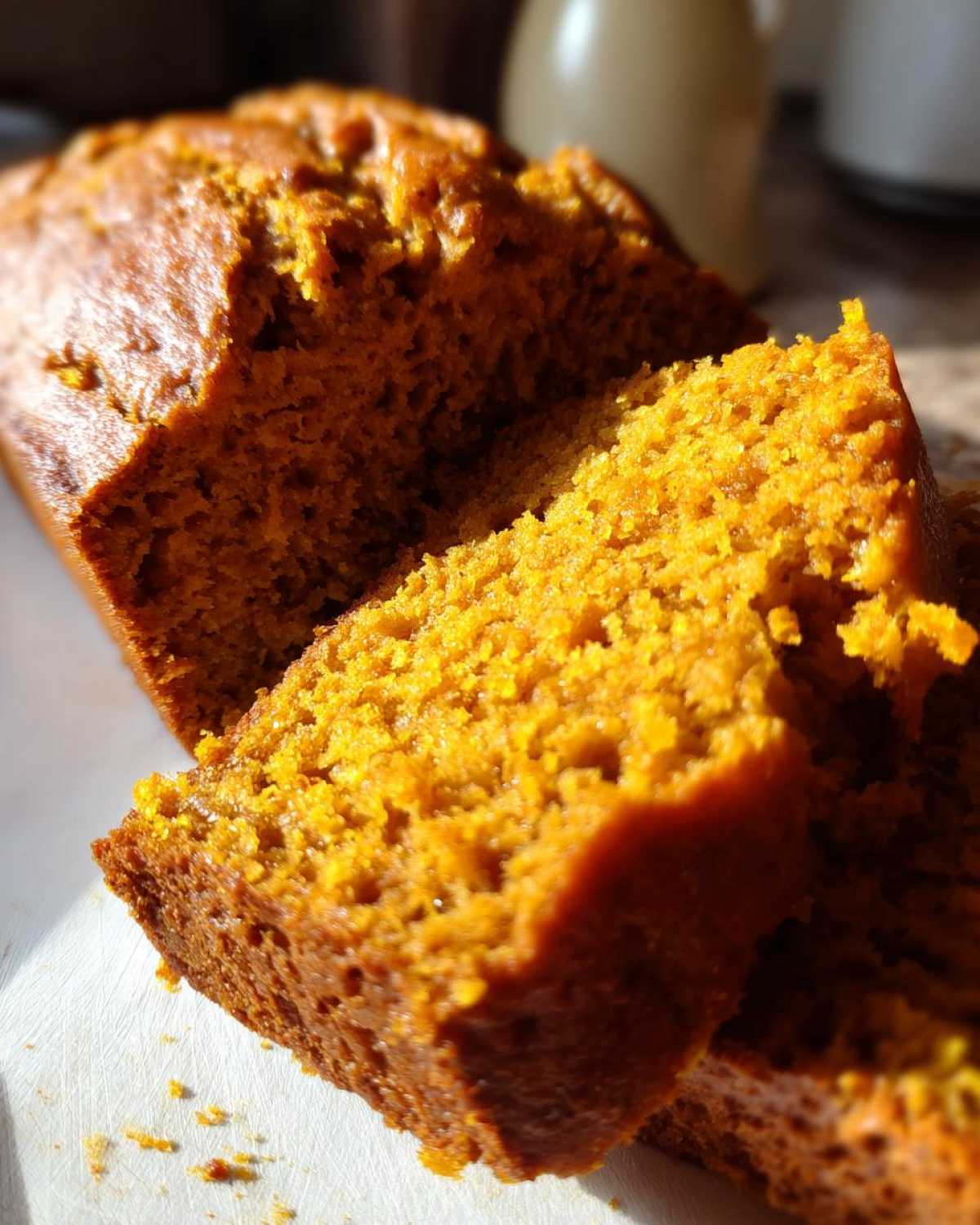 Close-up of moist, bright orange slices of homemade pumpkin bread on a white surface.