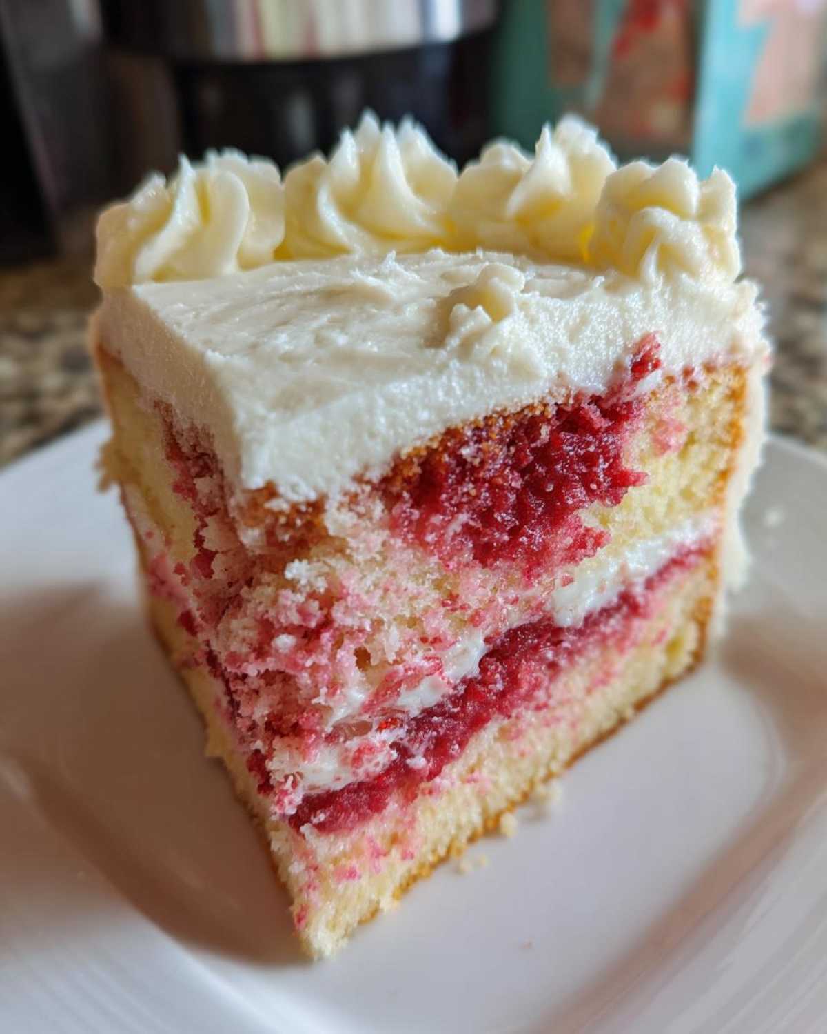 Close-up of a moist slice of strawberry cake with layers of pink filling and thick white frosting piped on top.