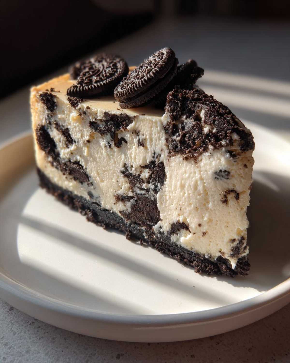 A rich slice of oreo cheesecake with chunks of cookies mixed in, topped with whole cookies.