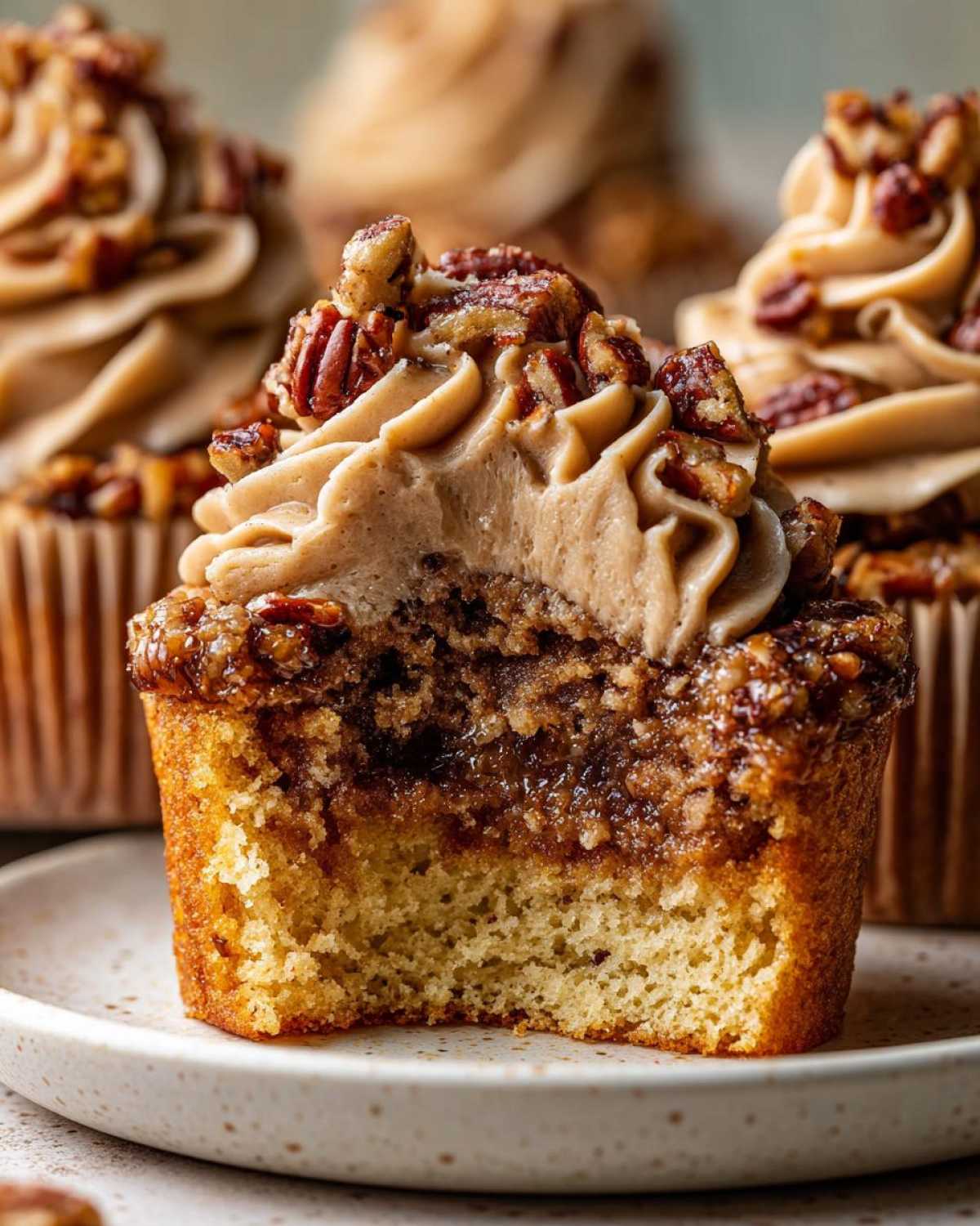 A close-up, cross-section view of a pecan pie cupcakes showing the cake base, gooey filling, and pecan-topped frosting.