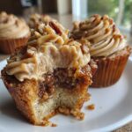 A pecan pie cupcake with a bite taken out, showing the gooey filling and caramel pecan frosting.