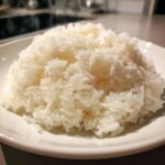 Close-up of fluffy, perfectly cooked sushi rice piled high on a white plate, ready for rolling.