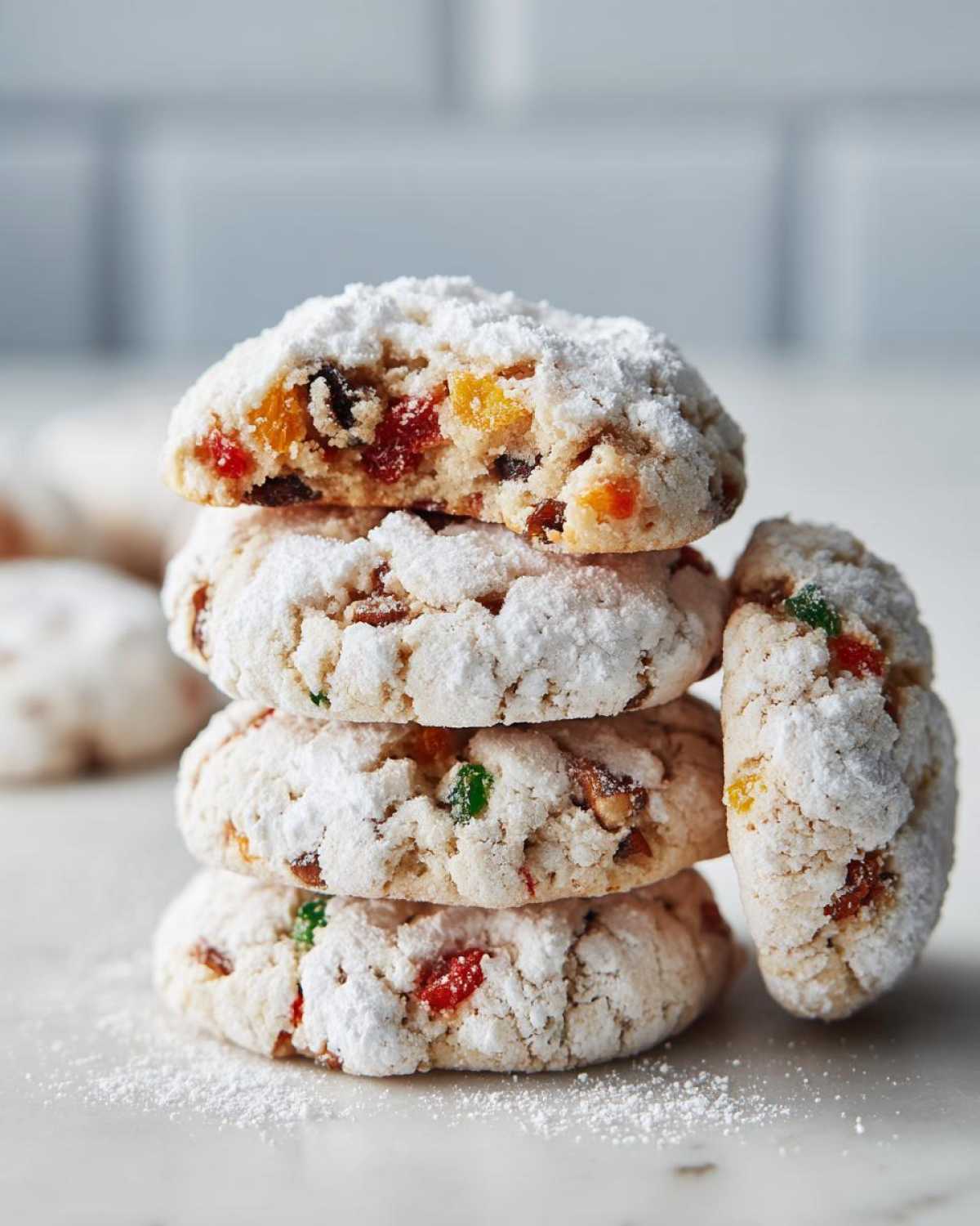 A stack of four delicious fruitcake cookies generously dusted with powdered sugar on a white marble surface.