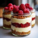 Close-up of a layered Protein Cheesecake jar topped with fresh raspberries and graham cracker crumble.