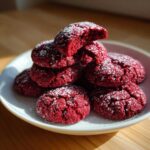 A stack of bright red velvet cake mix cookies dusted with powdered sugar on a white plate.