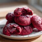 A stack of vibrant red velvet cake mix cookies dusted with powdered sugar on a white plate.
