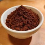 Close-up of rich, dark brown cocoa powder piled high in a small white bowl, ready for making hot cocoa mix.