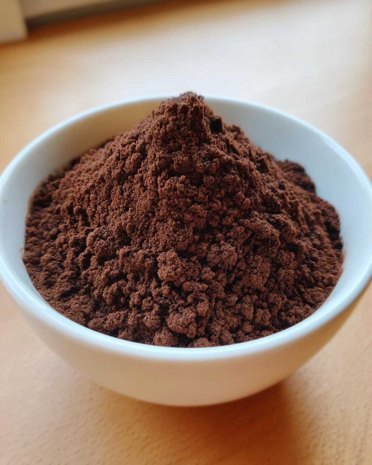 Close-up of rich, dark brown hot cocoa mix powder mounded high in a small white bowl.