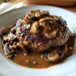 Close-up of a perfectly seared Salisbury steak smothered in thick, brown mushroom gravy.