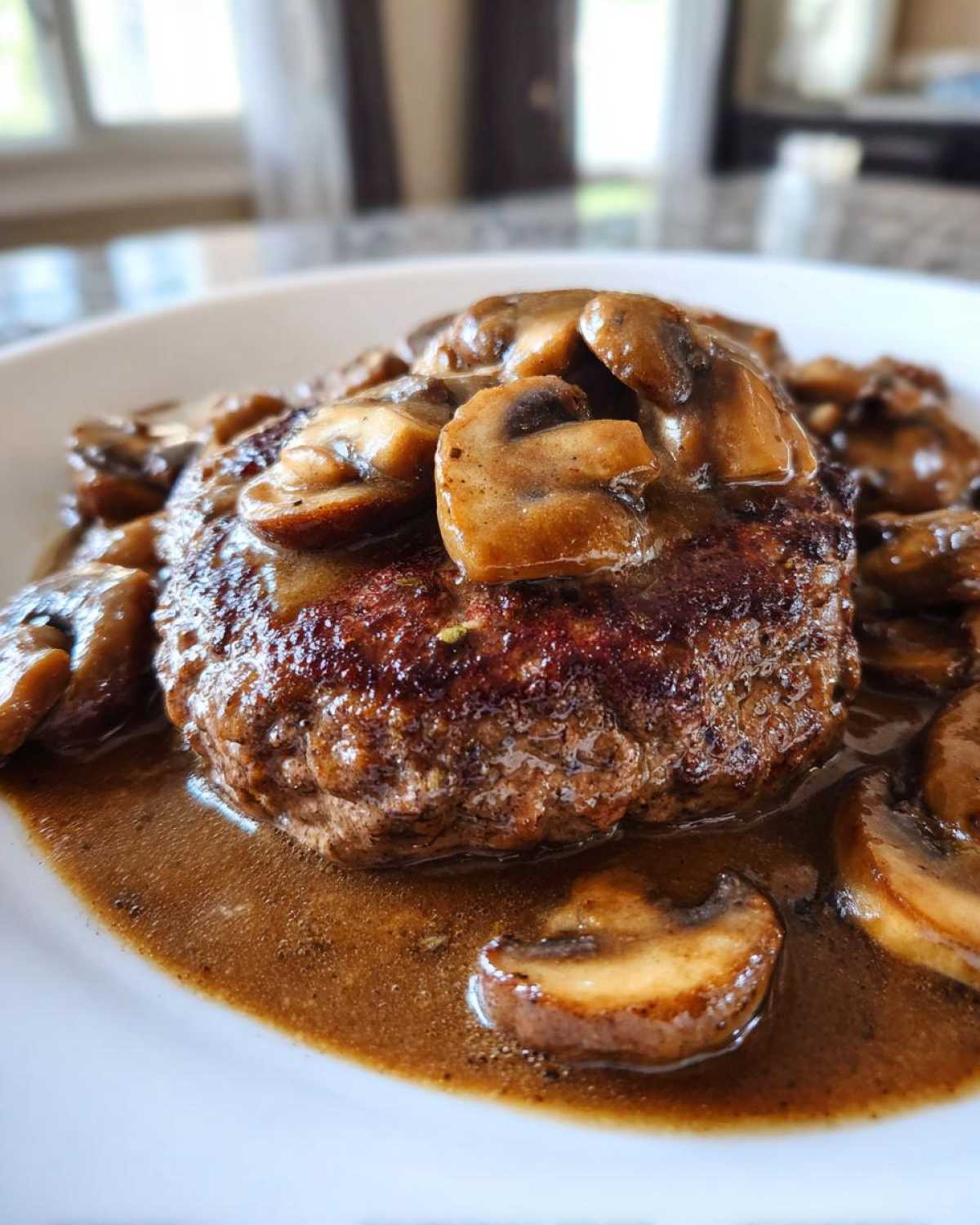 Close-up of a perfectly seared Salisbury steak smothered in rich brown mushroom gravy.