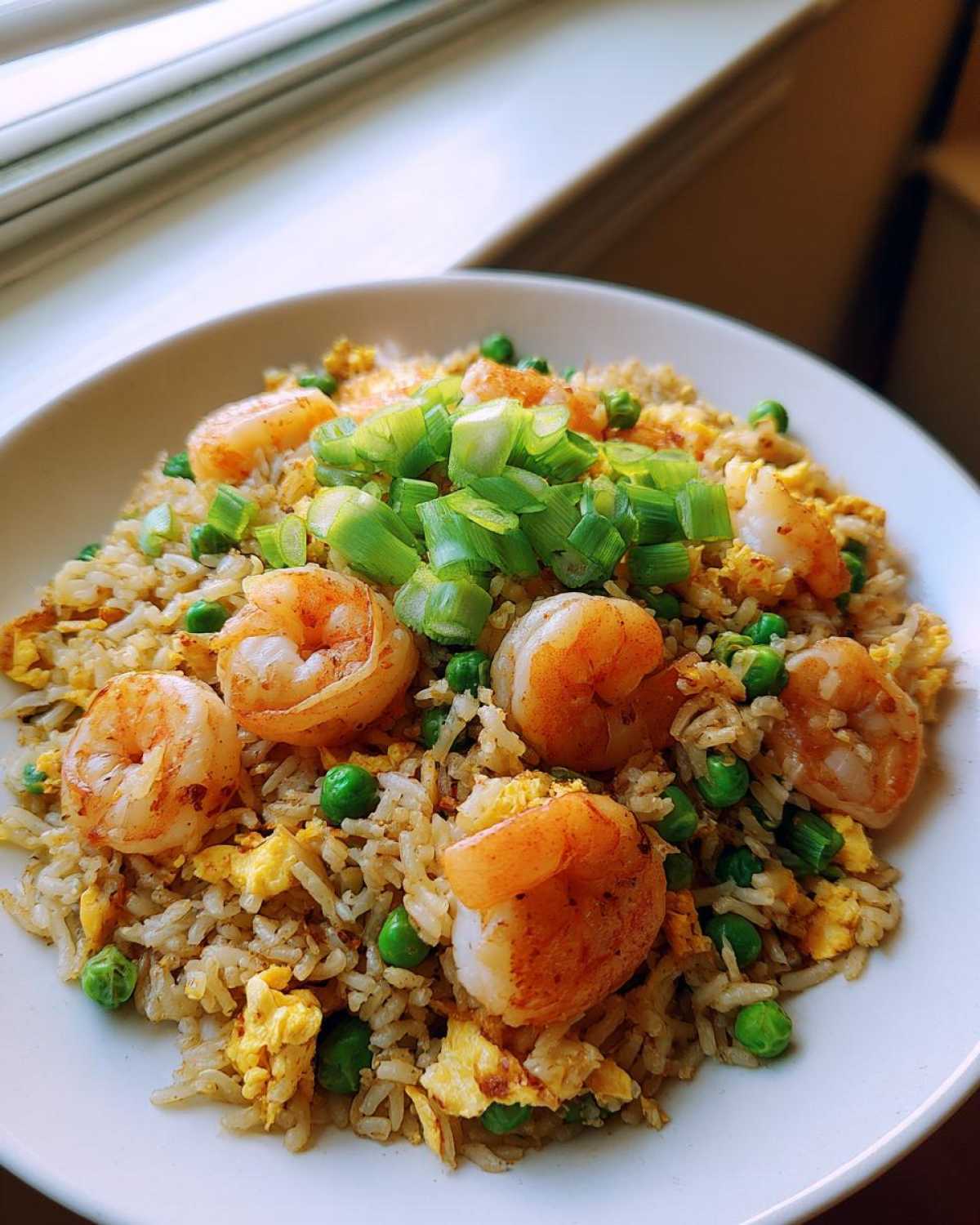 A close-up of delicious shrimp fried rice topped with large shrimp, green peas, scrambled egg, and fresh scallions.