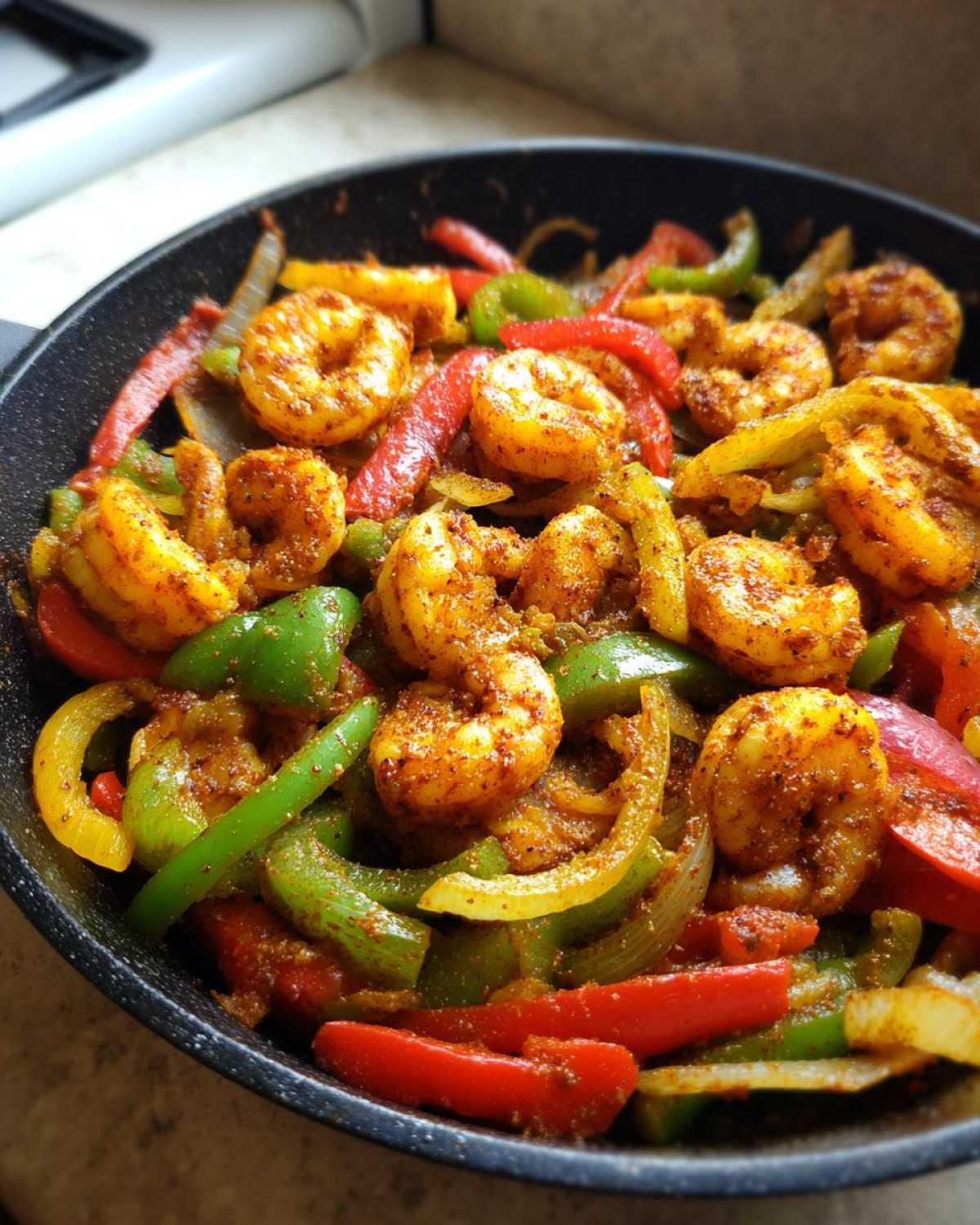 Close-up of seasoned shrimp mixed with colorful sliced bell peppers and onions cooking in a black skillet for shrimp fajitas.