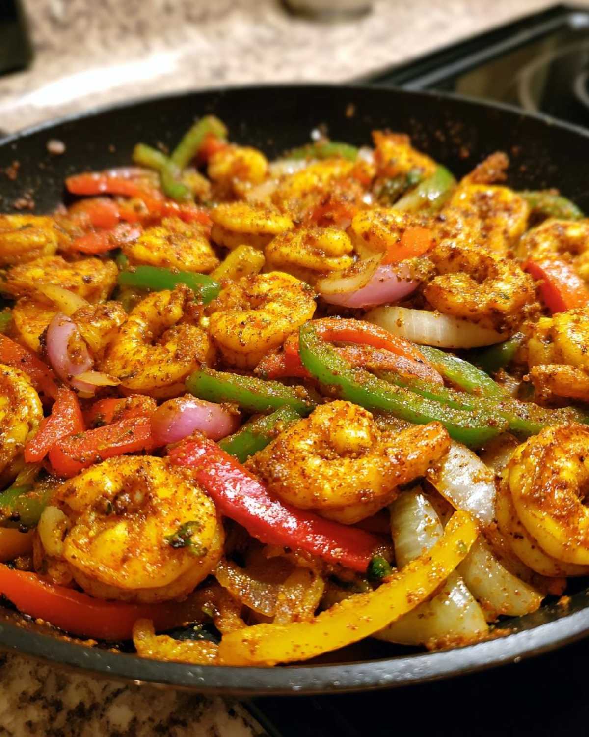 Close-up of seasoned shrimp fajitas cooking with colorful bell peppers and onions in a black skillet.