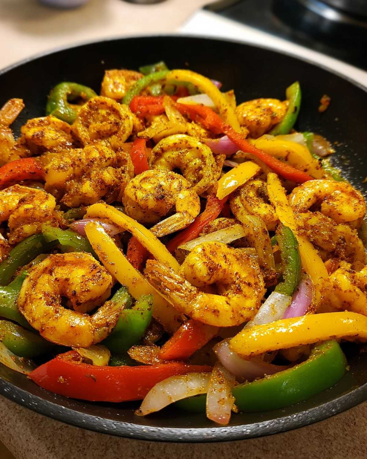 Close-up of seasoned shrimp fajitas cooking with colorful bell peppers and onions in a black skillet.