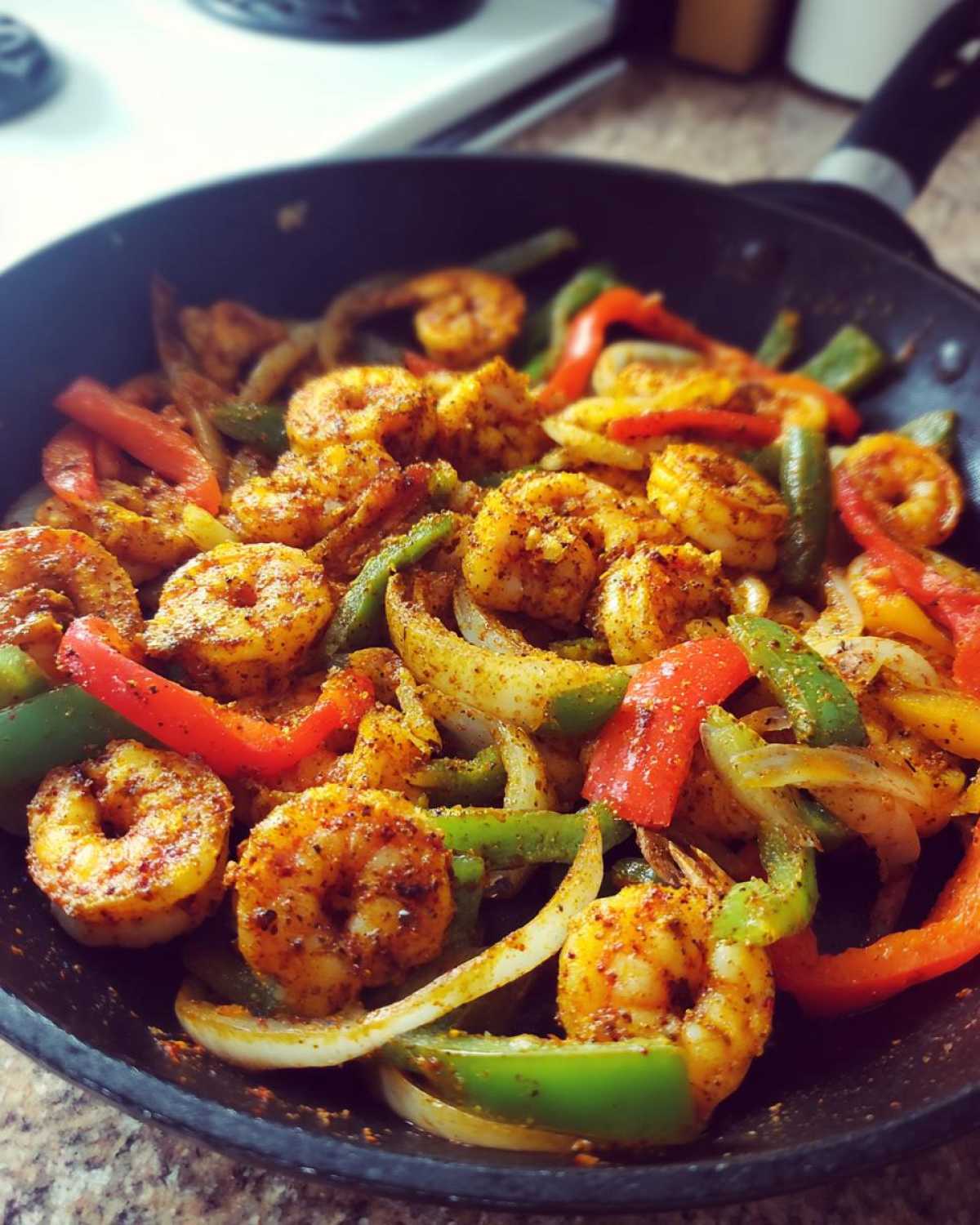 Close-up of seasoned shrimp fajitas cooking in a black skillet with colorful bell peppers and onions.
