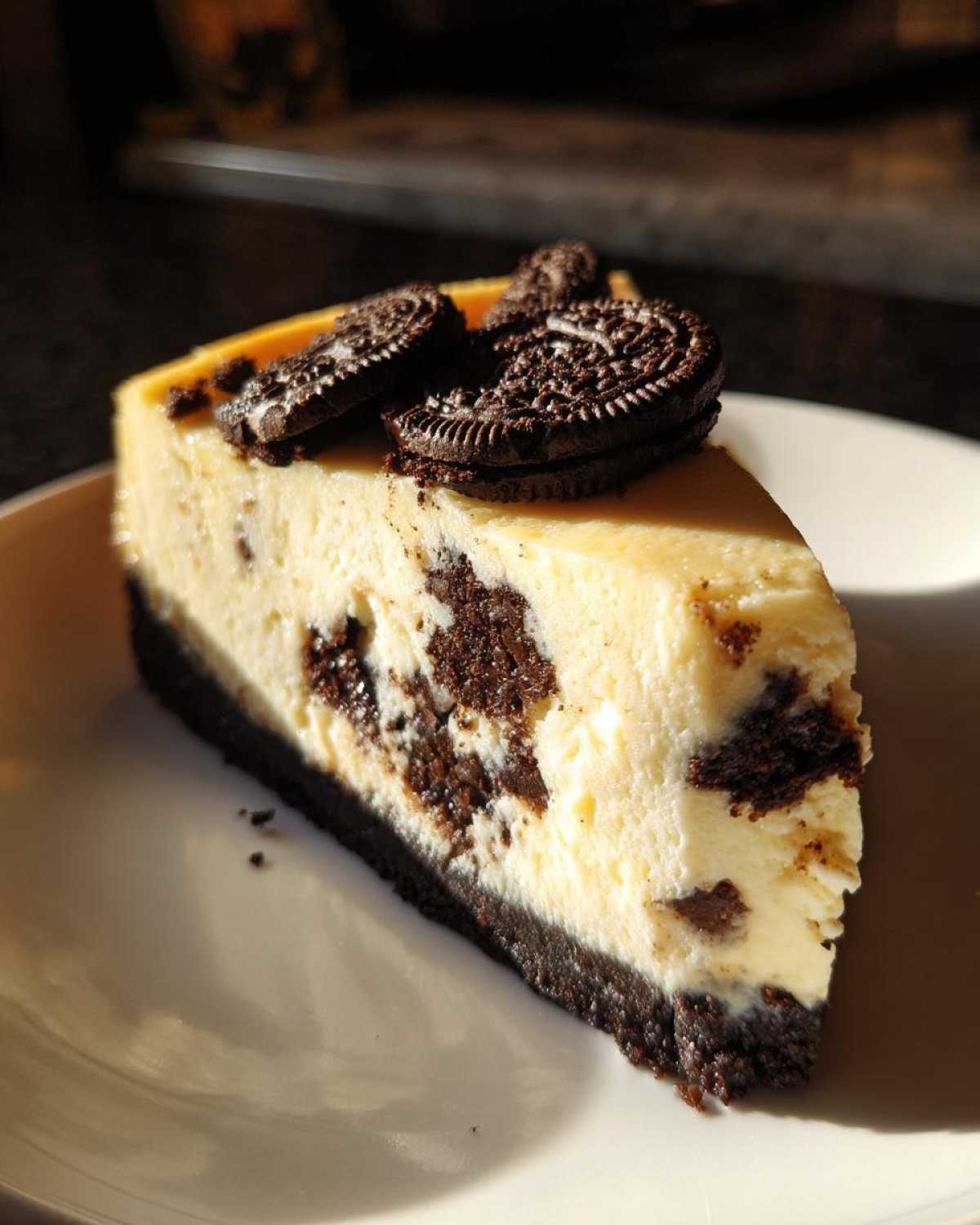 A decadent slice of oreo cheesecake featuring a dark chocolate crust and chunks mixed into the creamy filling, topped with mini Oreo cookies.