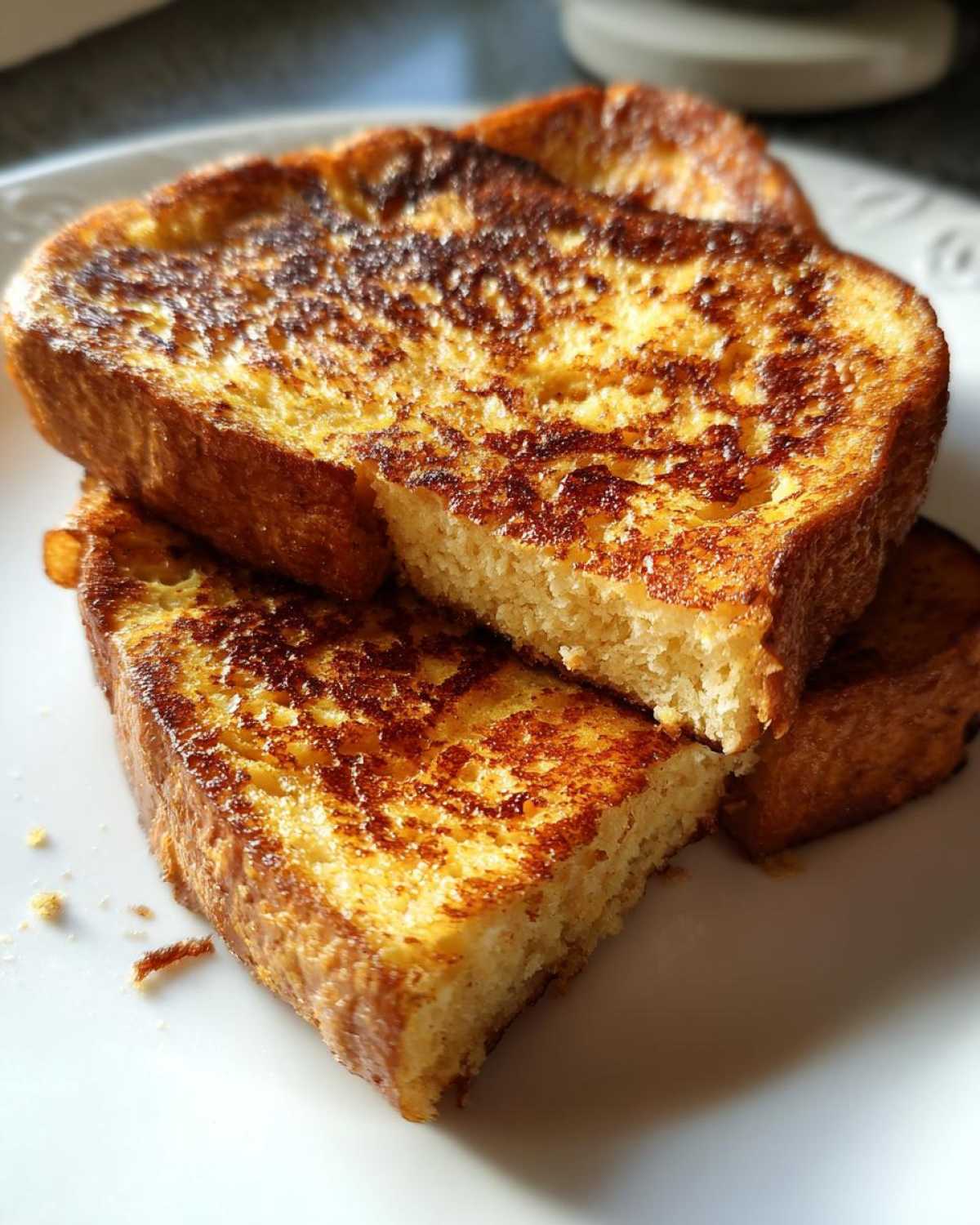 Close-up of thick slices of golden brown sourdough french toast stacked on a white plate.