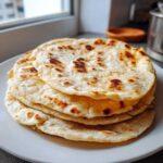 A stack of warm, slightly charred corn tortillas resting on a white plate.