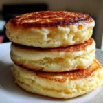 A close-up stack of three thick, fluffy pancakes with golden-brown, slightly crisp tops.