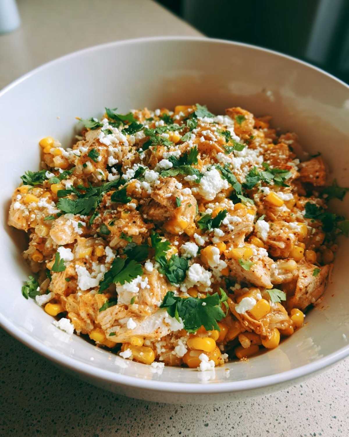 A close-up view of a street corn chicken rice bowl topped with crumbled white cheese and fresh cilantro.